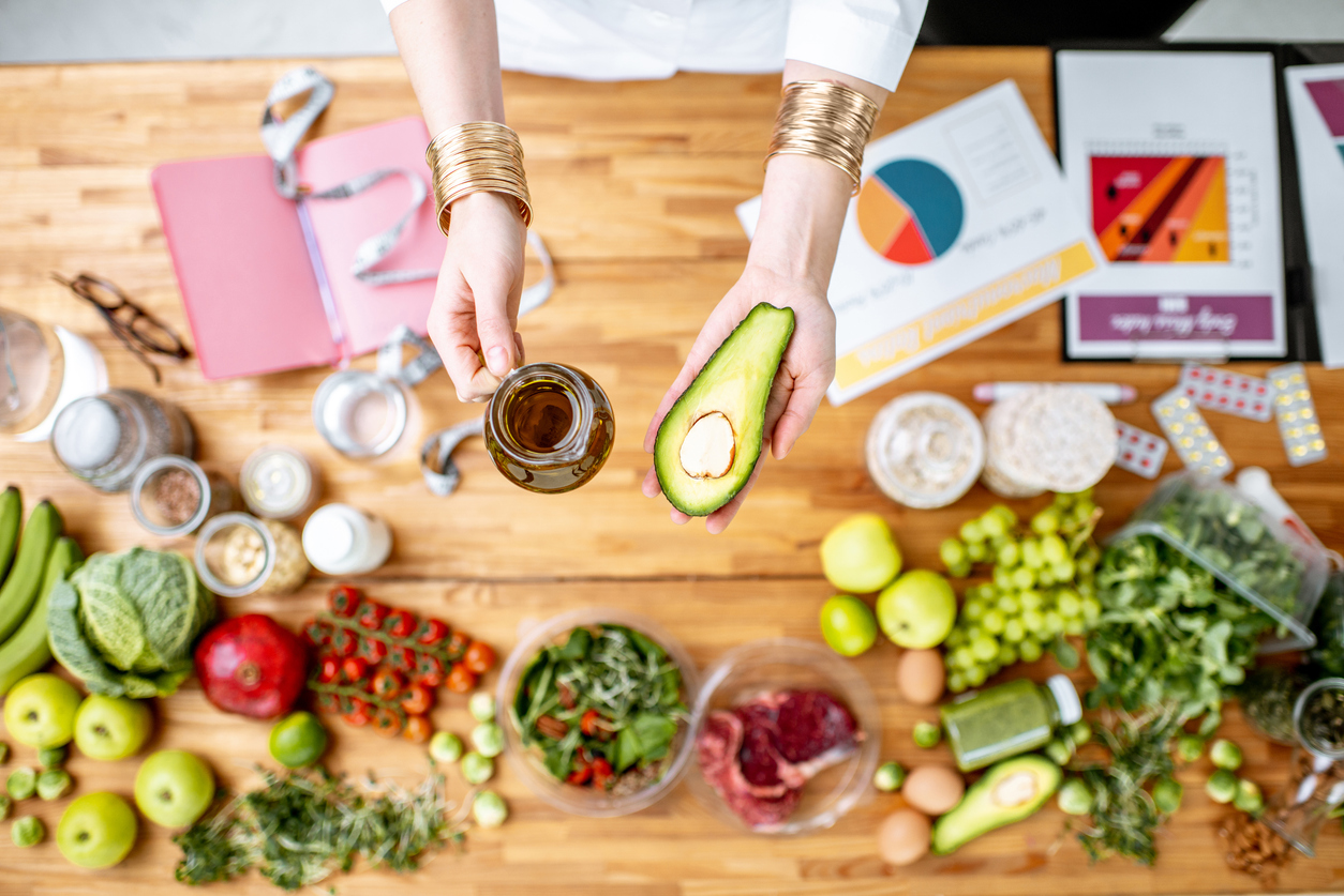 Dietitian holding avocado and olive oil above the table full of healthy food Dietitian holding avocado and olive oil above the table full of various healthy products, ketogenic diet concept