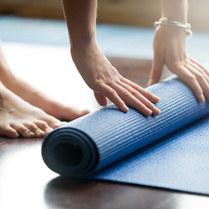 Yoga training concept Close-up of attractive young woman folding blue yoga or fitness mat after working out at home in living room. Healthy life, keep fit concepts. Horizontal shot